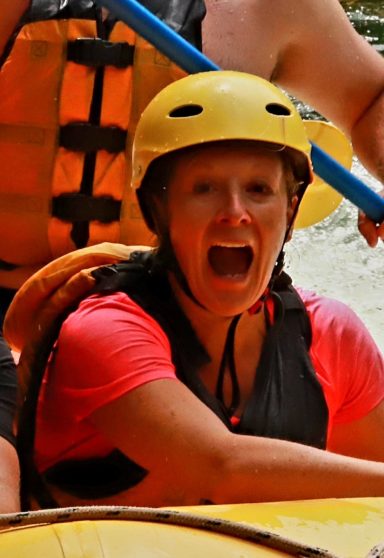 Lachende Person mit Helm beim Wildwasser-Rafting, zeigt Freude und Aufregung.
