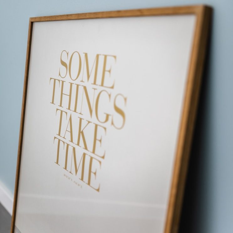 Ein gerahmtes Poster mit der Aufschrift "Some things take time" in goldener Schrift.