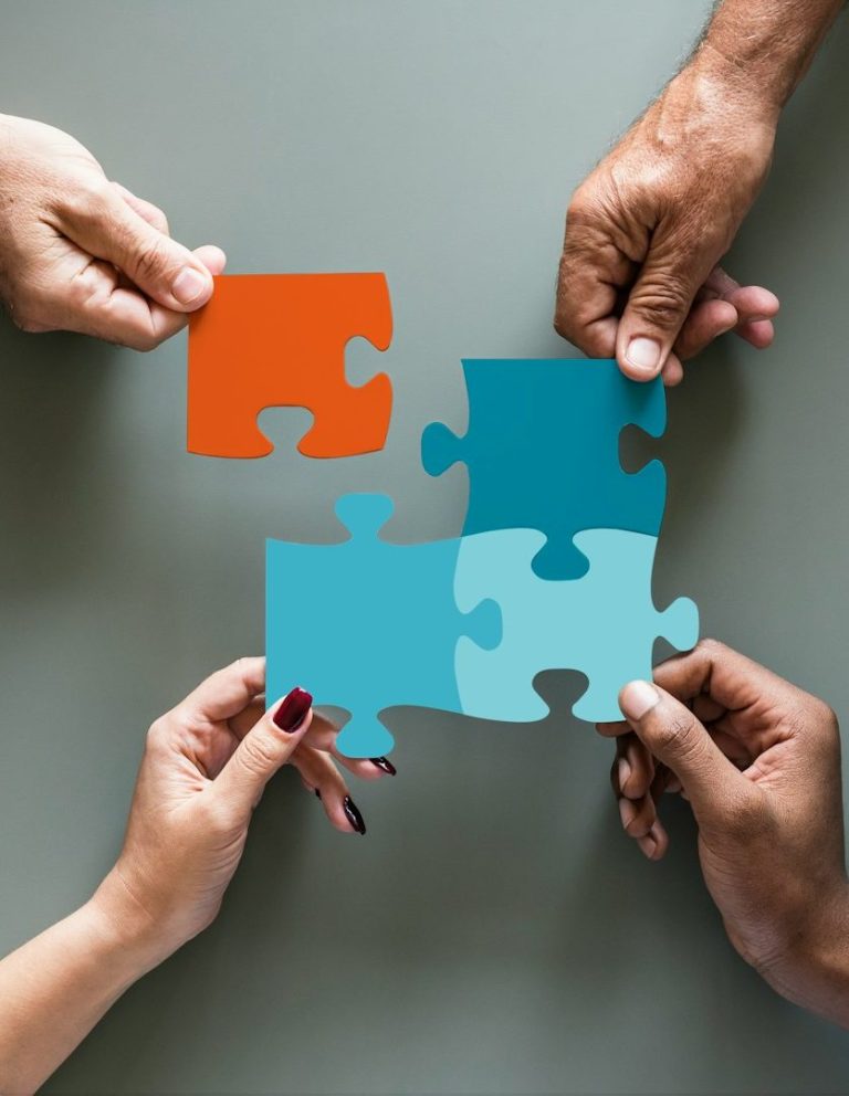 Hände halten farbige Puzzlestücke in orange und blau, die zusammengefügt werden.