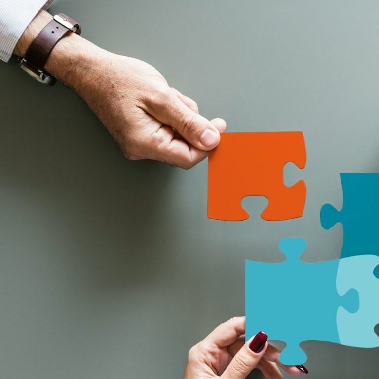 Hände halten farbige Puzzlestücke, die zusammengefügt werden.