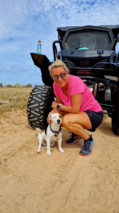 Frau in pinkem Shirt posiert mit einem kleinen Hund neben einem Geländewagen.