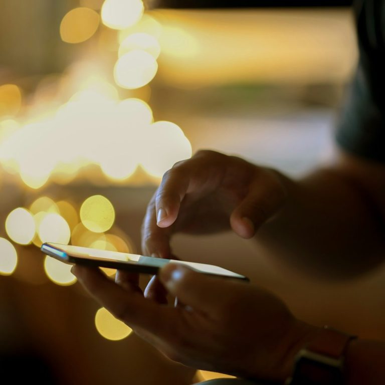 Eine Hand tippt auf einem Smartphone, umgeben von verschwommenem Licht.