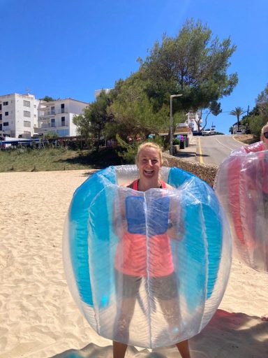Frau steht auf einem Strand in einer transparenten, farbigen Bubble-Statue.