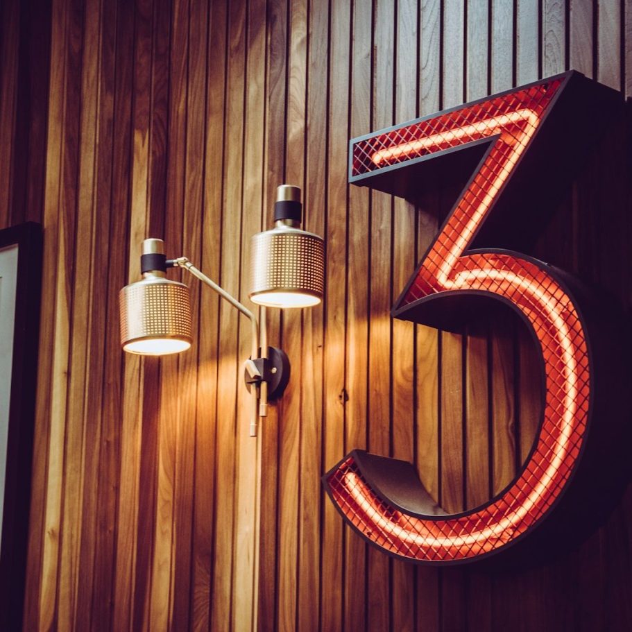 Leuchtende rote Zahl drei an einer Holzpaneelwand mit zwei Lampen.